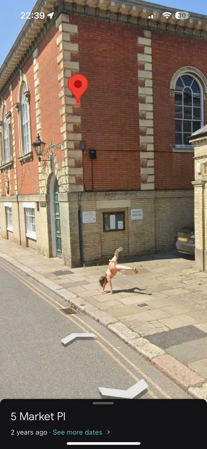A person performing a handstand on a sidewalk next to a brick building, a bizarre Google Street View moment.