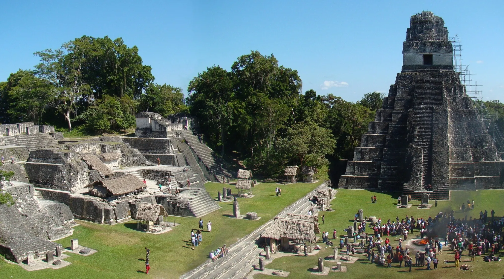 Tikal's ancient Mayan citadel, featuring iconic pyramids, stone structures, and a large gathering of people on grassy grounds.