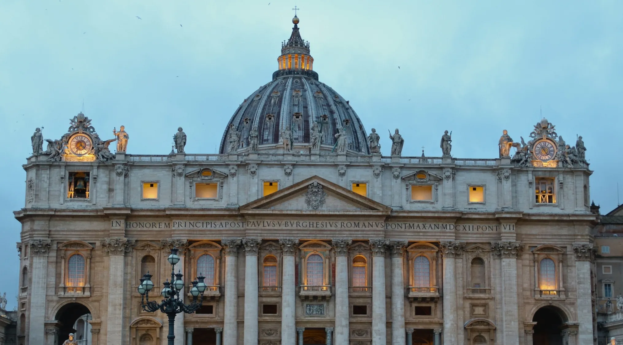 St. Peter's Basilica, an iconic church with its grand dome and facade, illuminated at dusk. Guess the country.