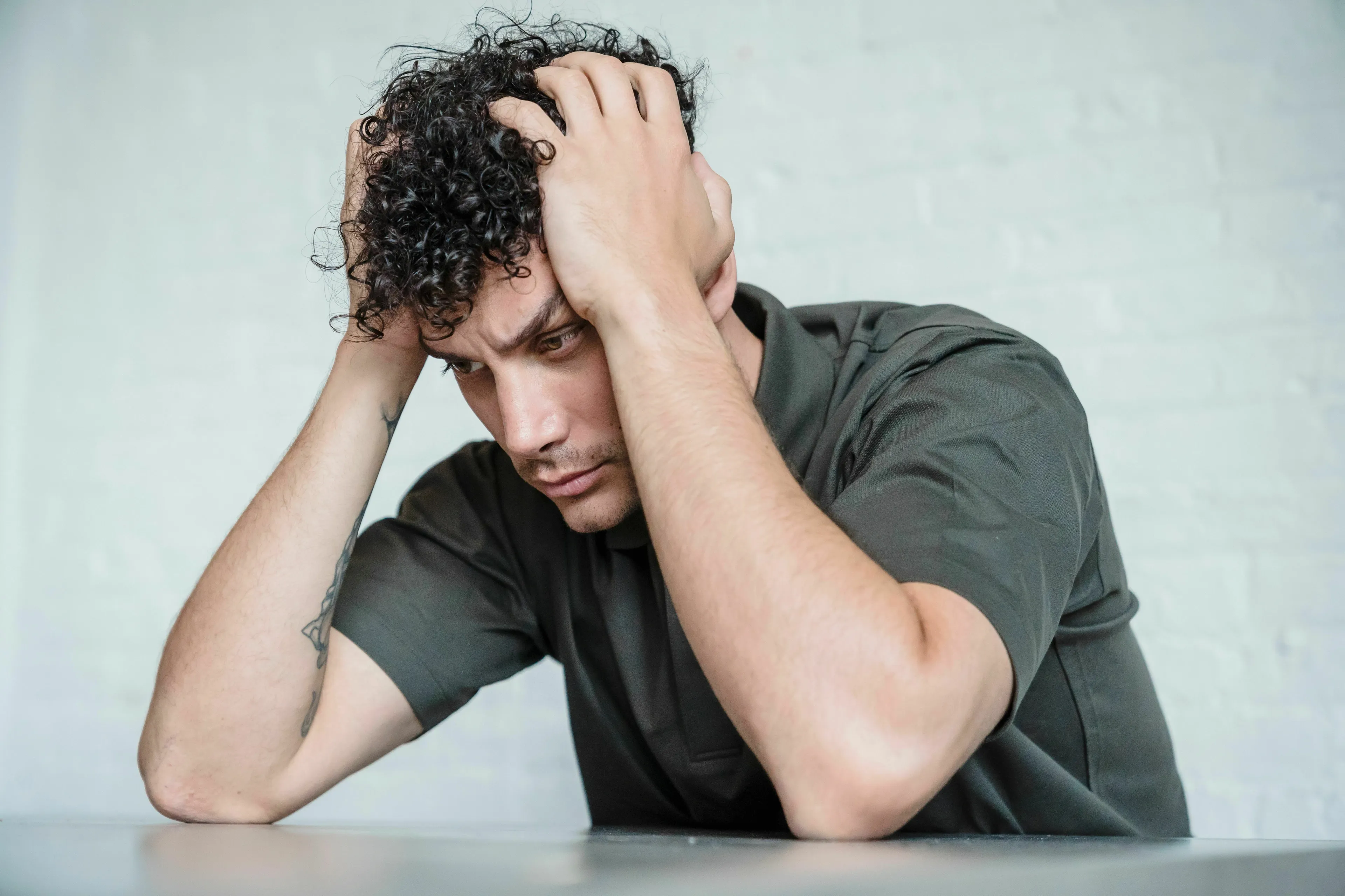 A man with curly hair holds his head in his hands, looking stressed the night before something big, questioning his bravery.