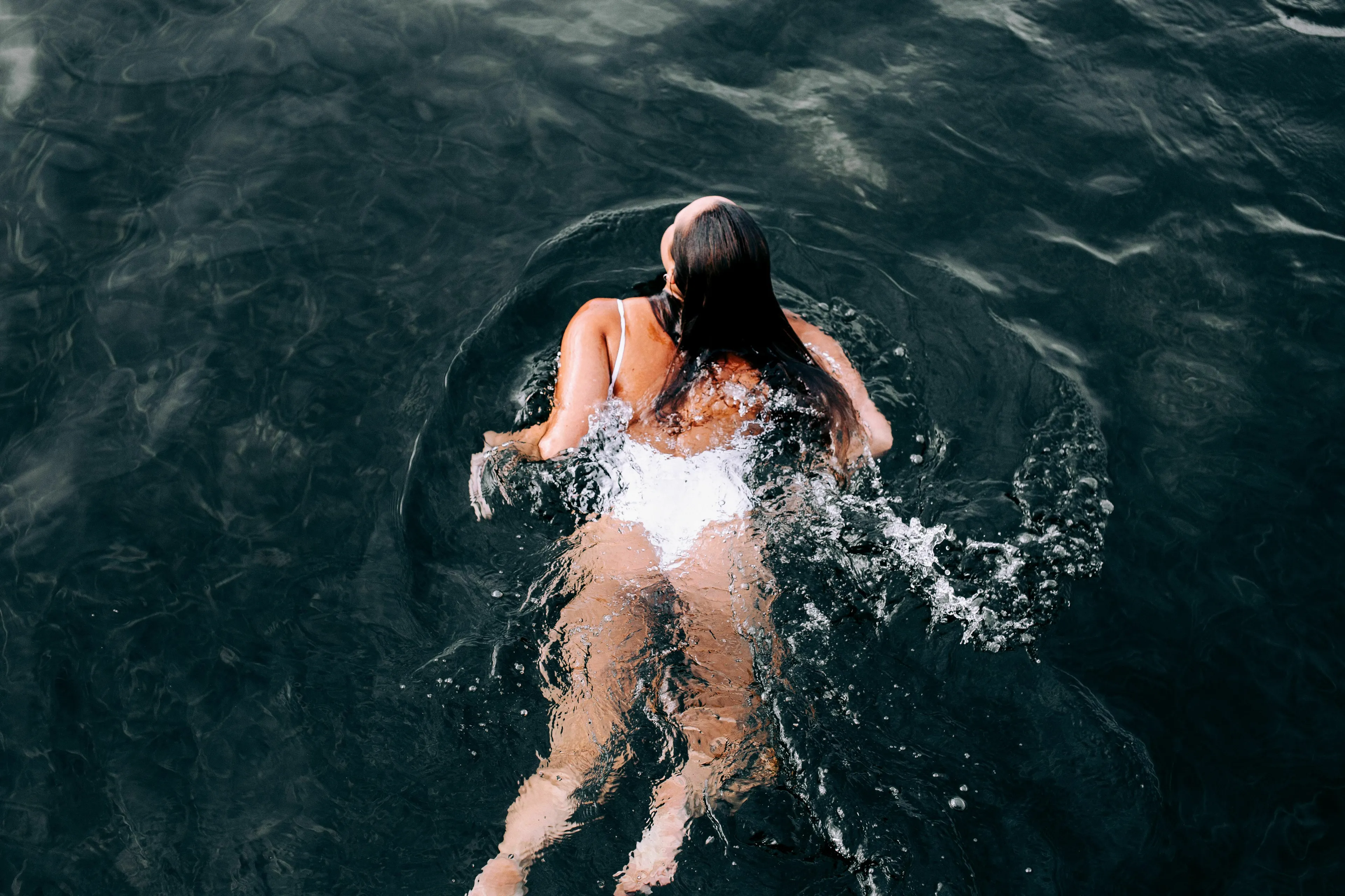 A woman swimming in dark water, looking up, having drifted further out than planned.