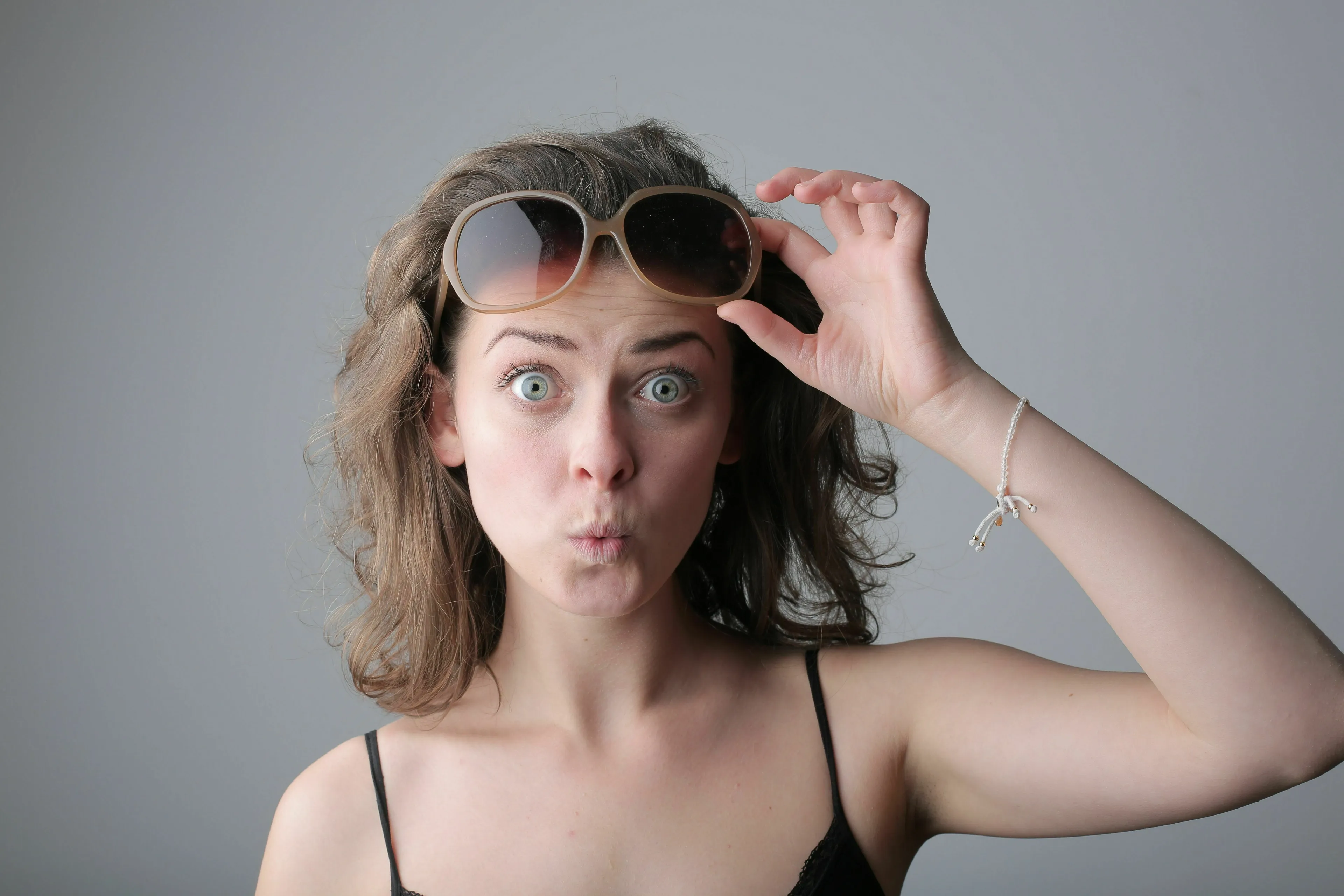 A surprised woman with wide eyes and open mouth, holding up sunglasses. A brave person.