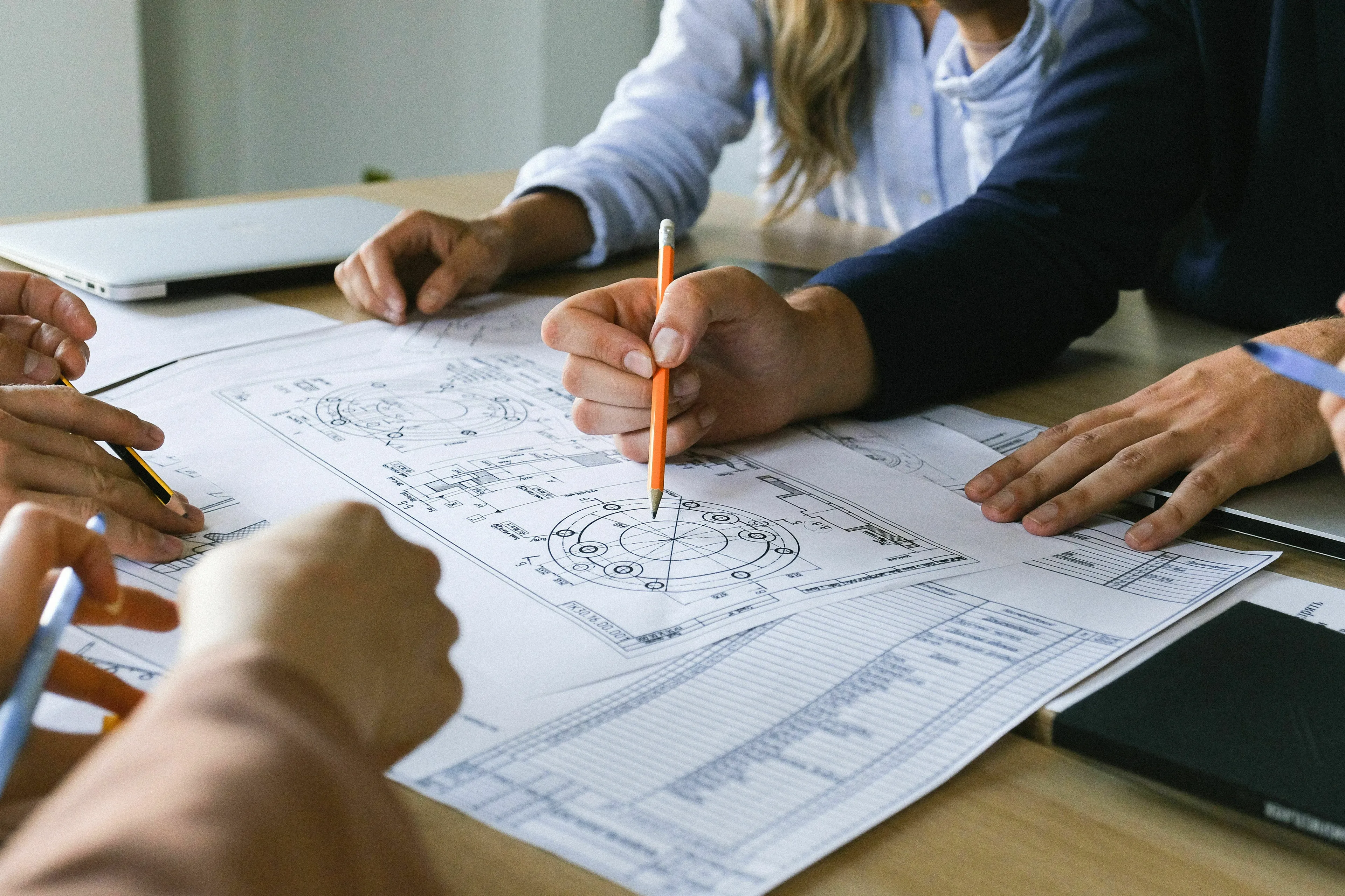 People collaborating around a table, hands pointing at a blueprint, depicting starting a big project.