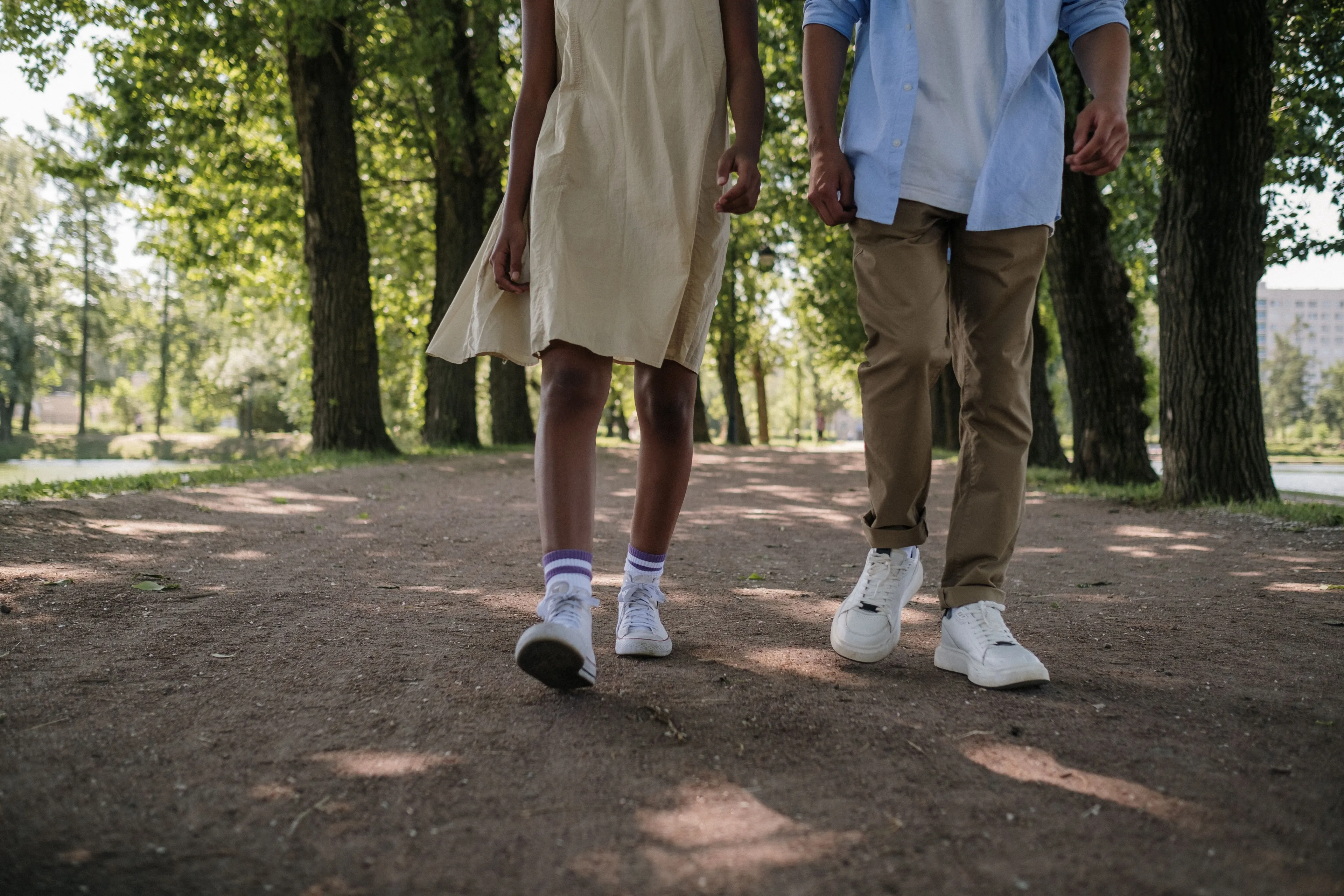A walk in the park; two people walking on a dirt path surrounded by trees, enjoying a weekend activity.