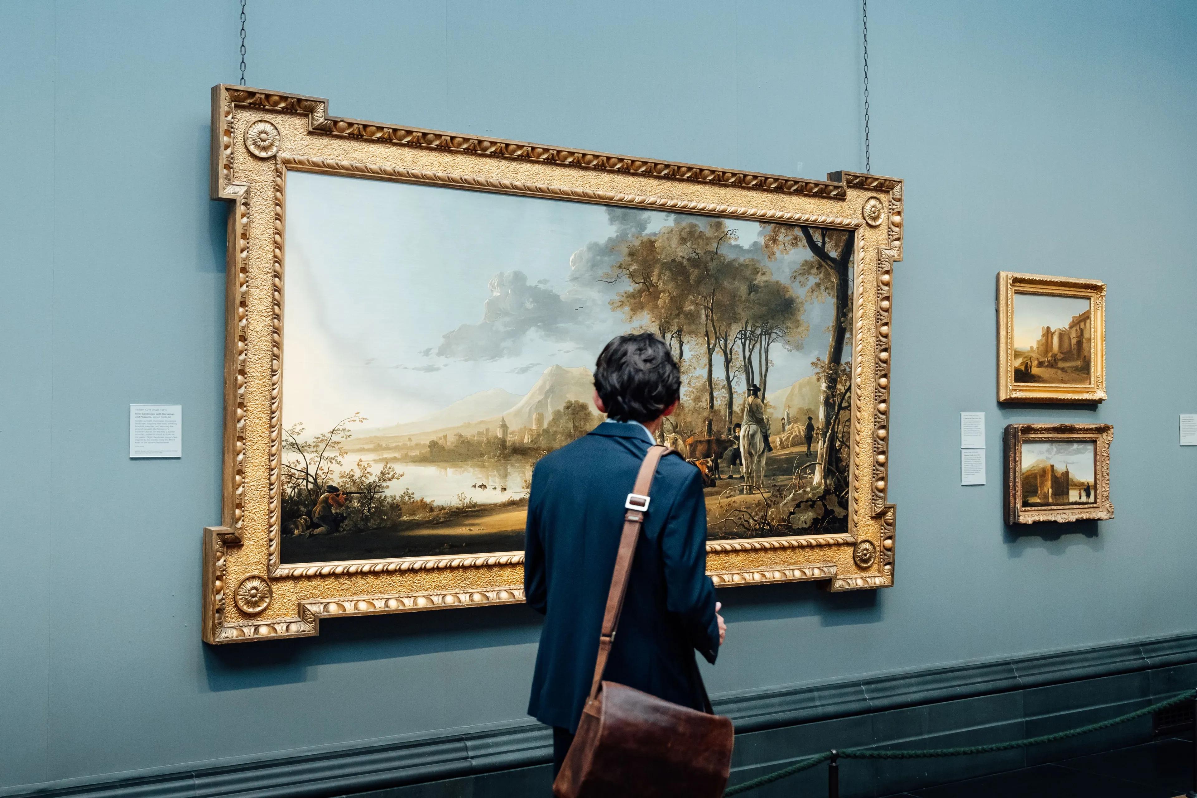 A person viewing a large, framed landscape painting in a museum, a cultural weekend activity.