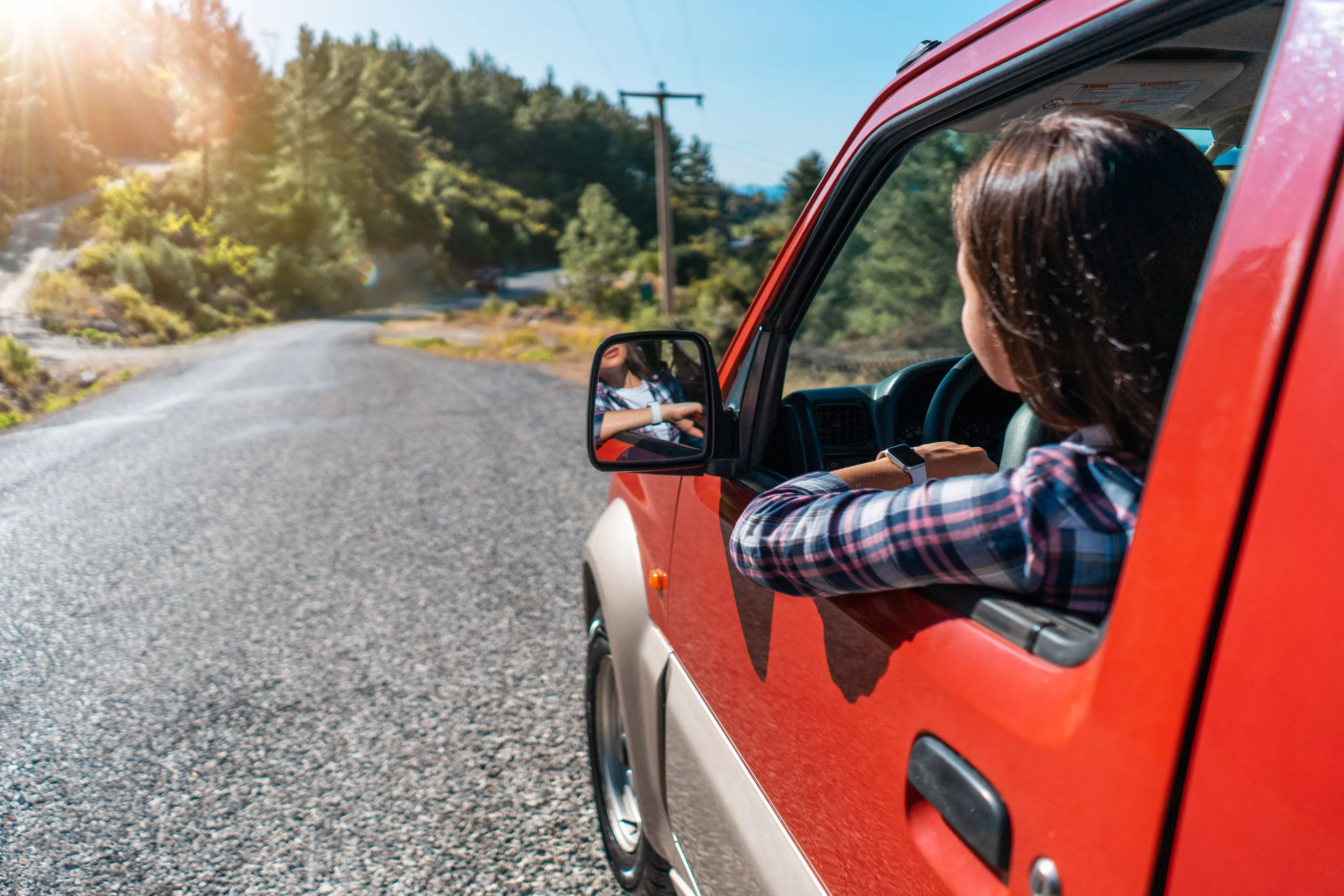 A woman driving a red car on a scenic road, embarking on a road trip adventure for the weekend.