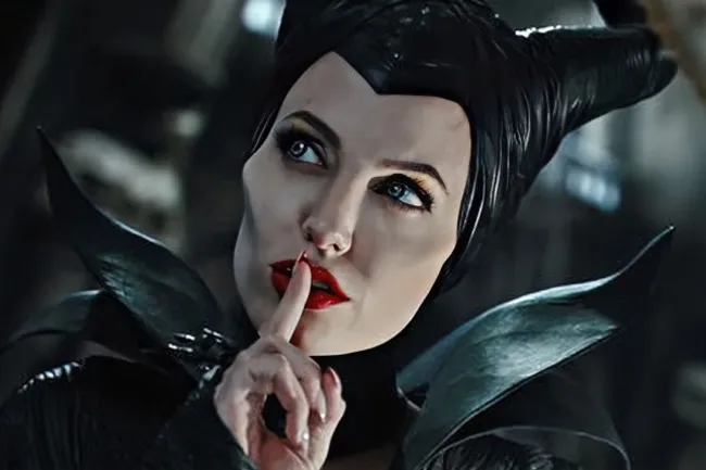 A close-up of Maleficent, a movie villain, in costume, with a finger to her lips.