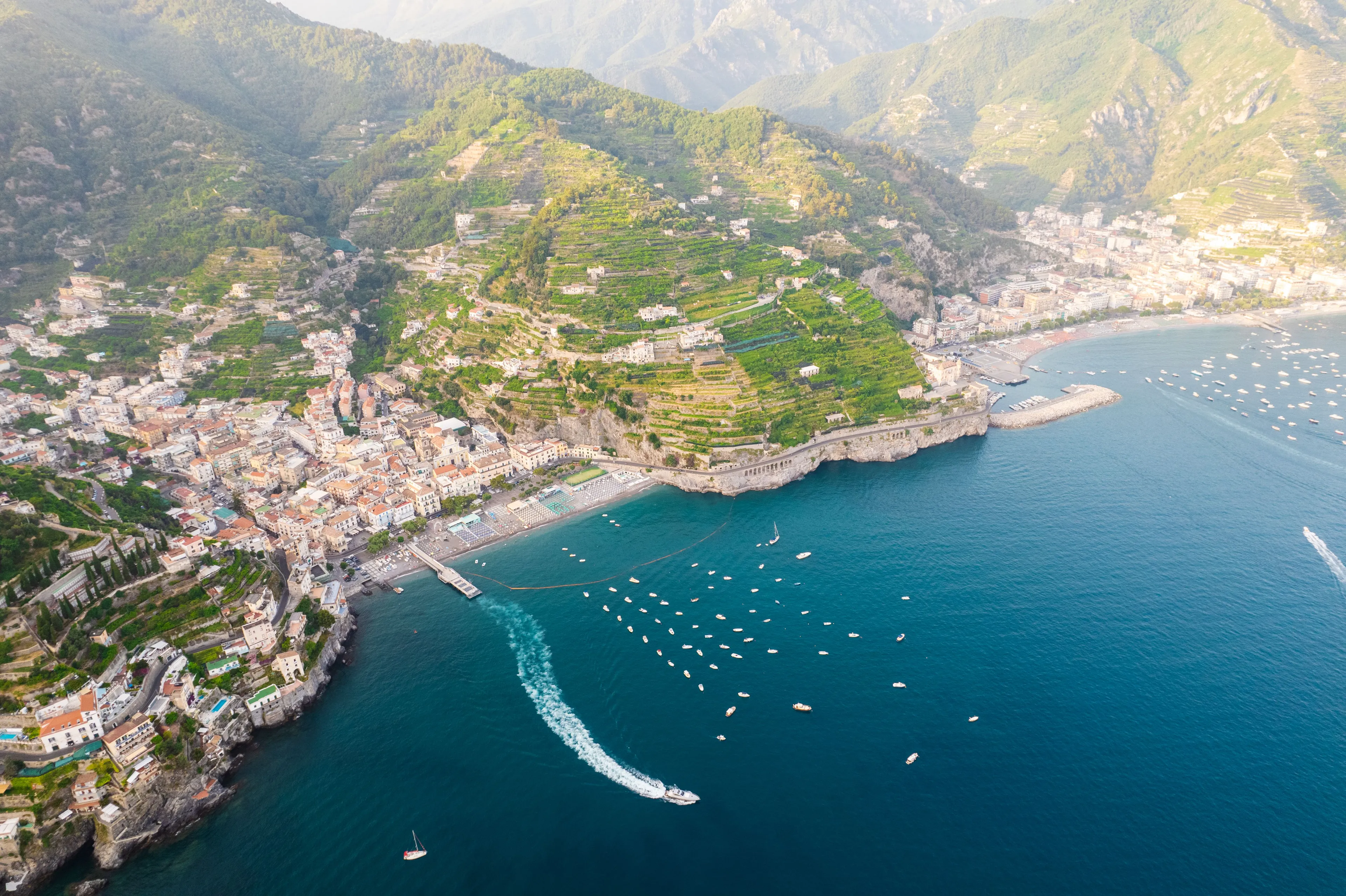 An aerial view of the stunning Amalfi Coast with its colorful towns, terraced hillsides, and boats on the blue sea.