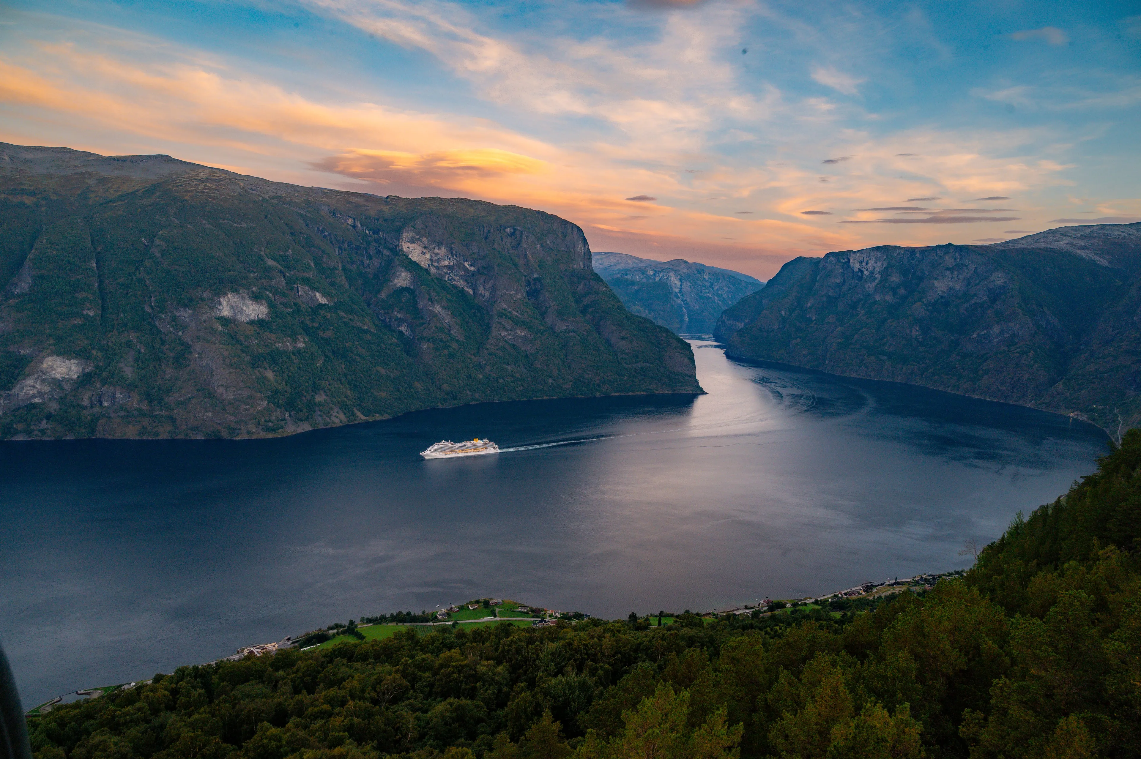 A majestic Norwegian Fjord with a cruise ship sailing through the calm waters, surrounded by towering mountains.