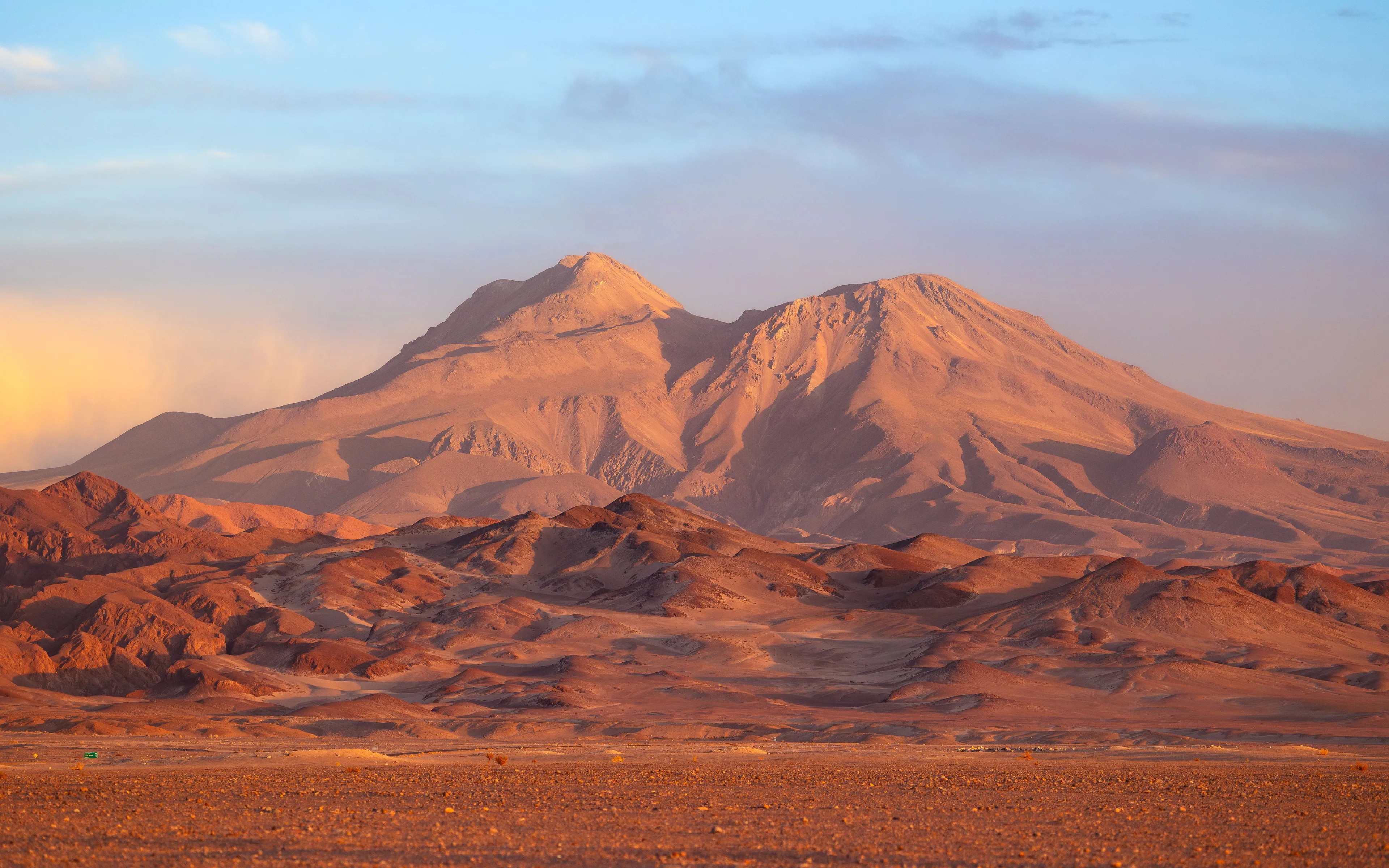 The vast, arid landscape of the Atacama Desert, featuring a large, imposing mountain range under a clear sky.