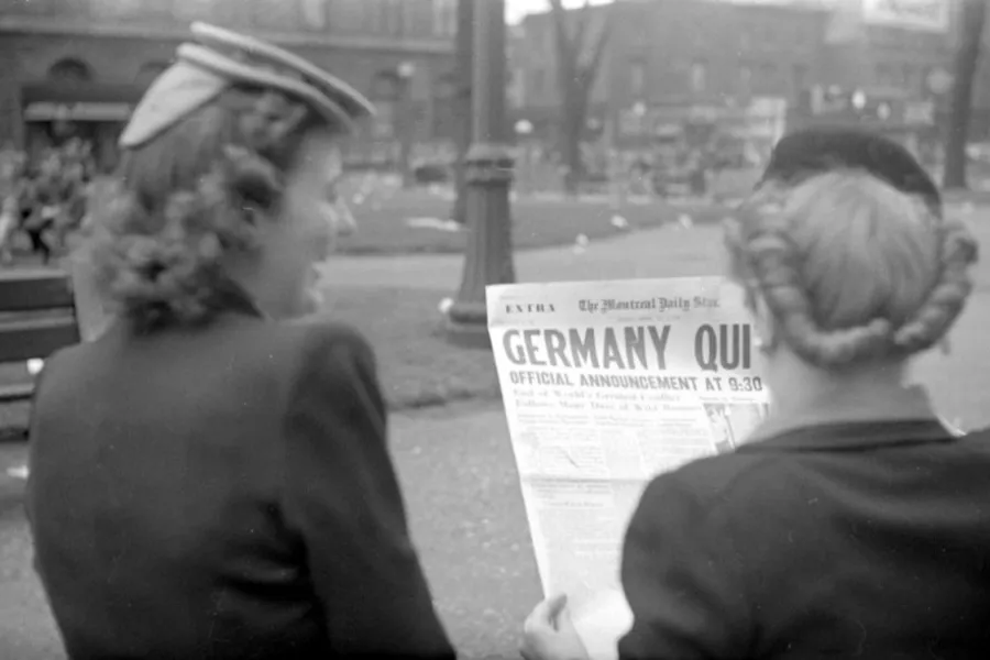 Two women reading a newspaper with the headline Germany Quit, signifying the end of WWII.