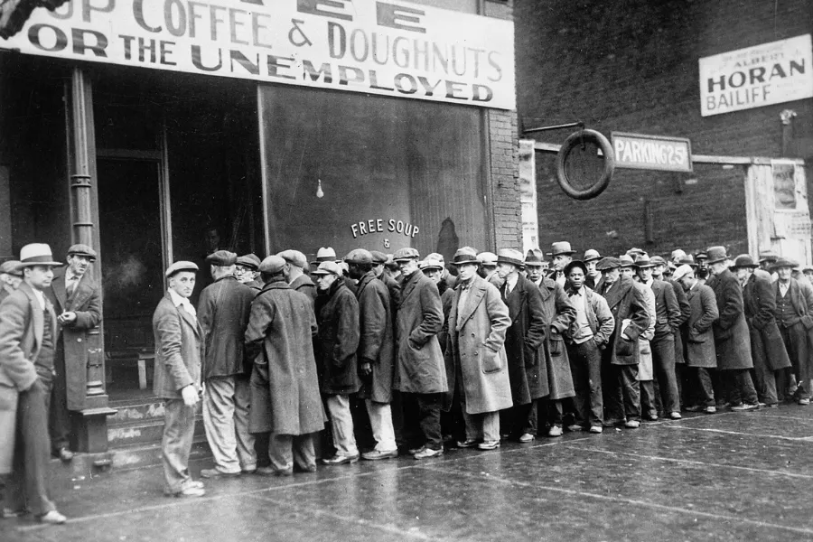 A long line of men in hats and coats outside a building offering free soup, depicting the Great Depression begins.
