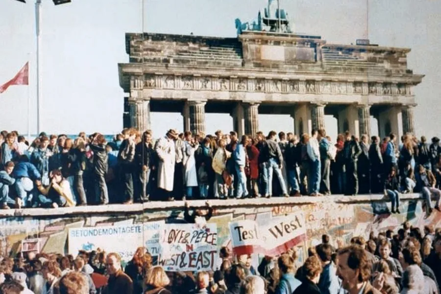 Crowds of people gather atop and around the Berlin Wall falls, near the Brandenburg Gate.