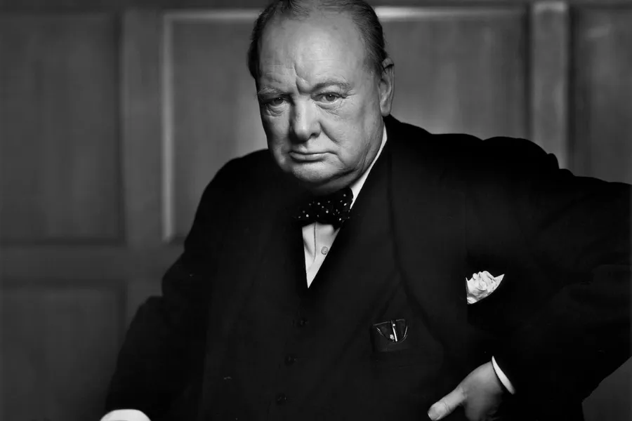 A black and white portrait of Churchill looking directly at the camera. He is wearing a suit and bow tie.
