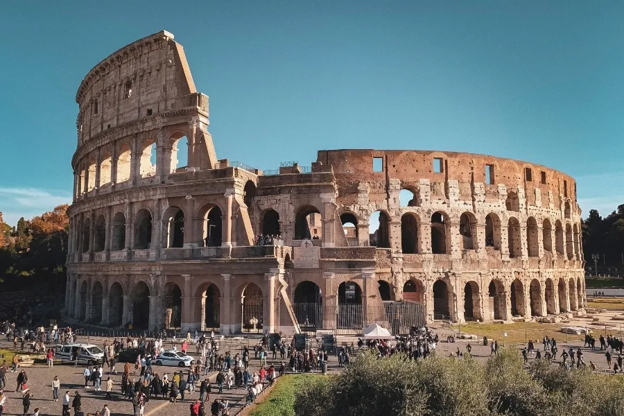 The ancient Roman Colosseum with many tourists walking around it under a clear sky.