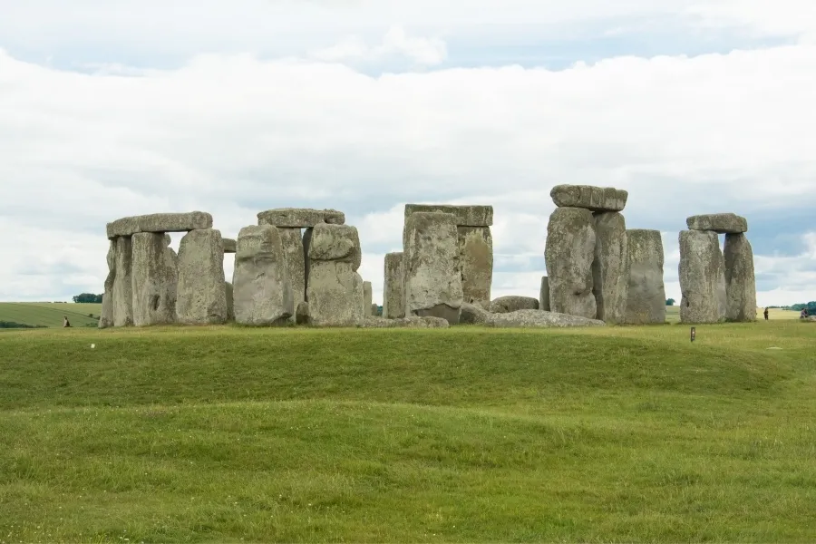 Massive prehistoric Stonehenge construction stands in a green field under a cloudy sky.