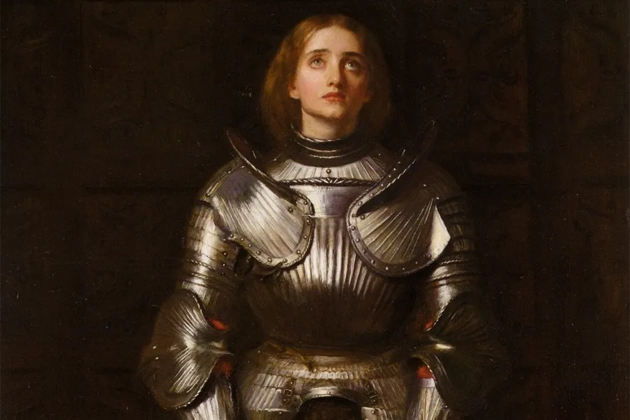 A painting of Joan of Arc in shining armor, looking upwards with a pensive expression against a dark background.