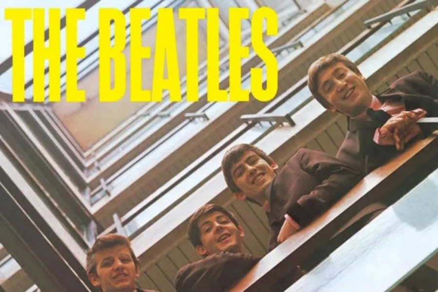 The Beatles album cover showing the four band members looking down from a balcony, with yellow text The Beatles.