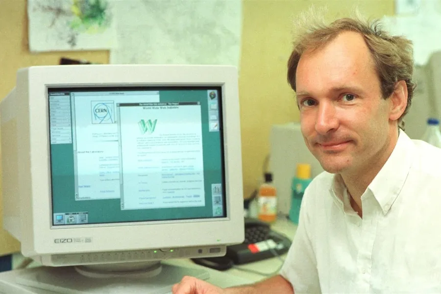 Tim Berners-Lee, the inventor of the World Wide Web, smiling at his desk with an early web browser on a computer monitor.