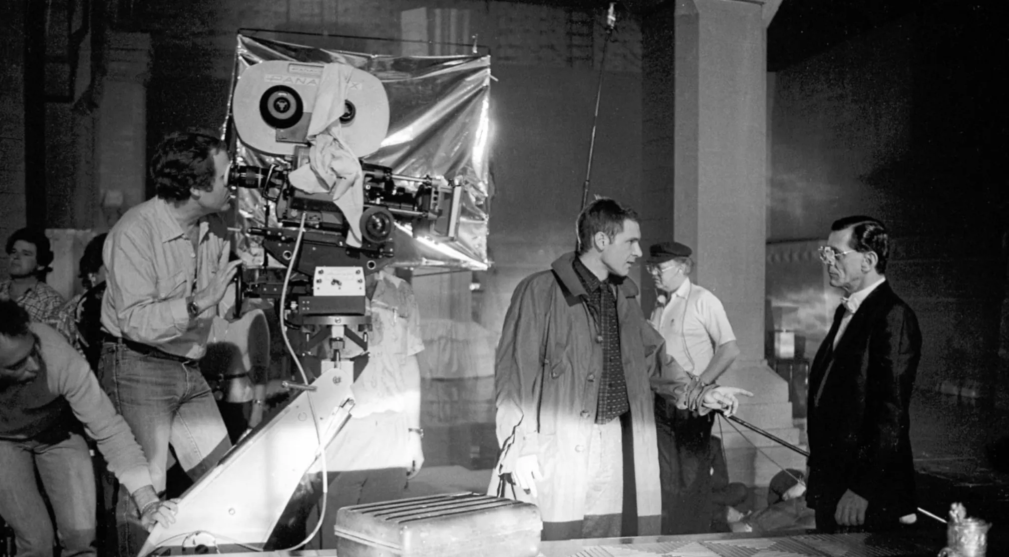 Black and white behind-the-scenes photo of crew members filming a movie scene. This is a 80s & 90s General Movie Trivia question.