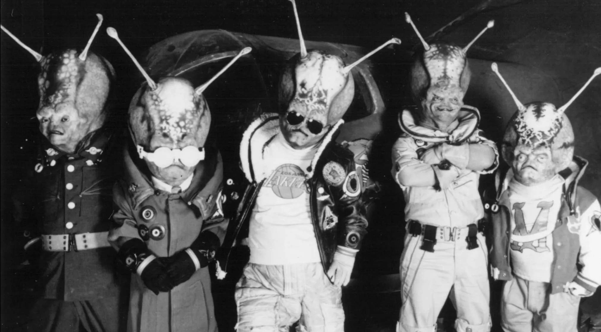 Black and white photo of five aliens with large heads and antennas, dressed in various movie trivia costumes.