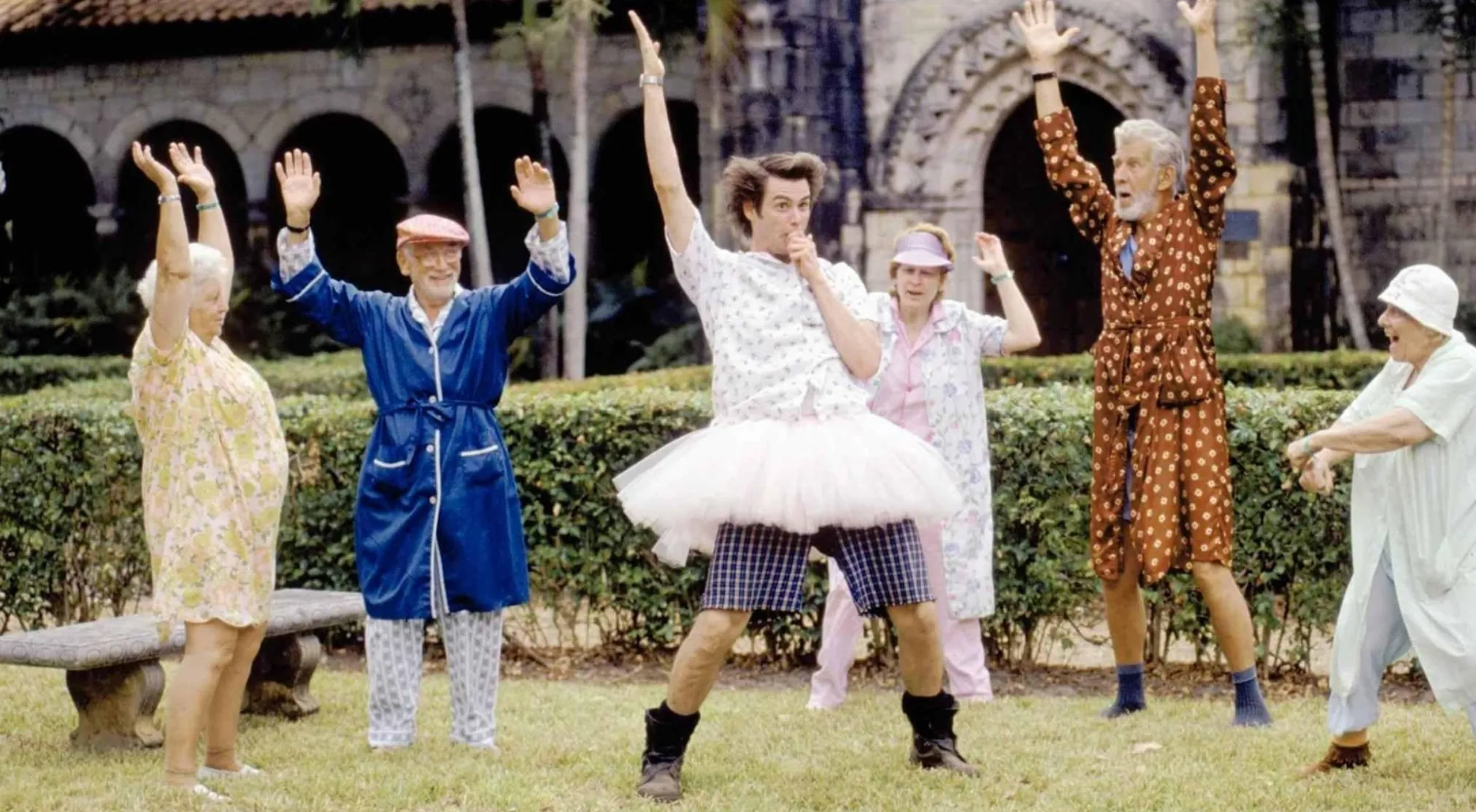 A comedic movie scene featuring Jim Carrey in a tutu, surrounded by seniors stretching. Perfect for 80s & 90s movie trivia.