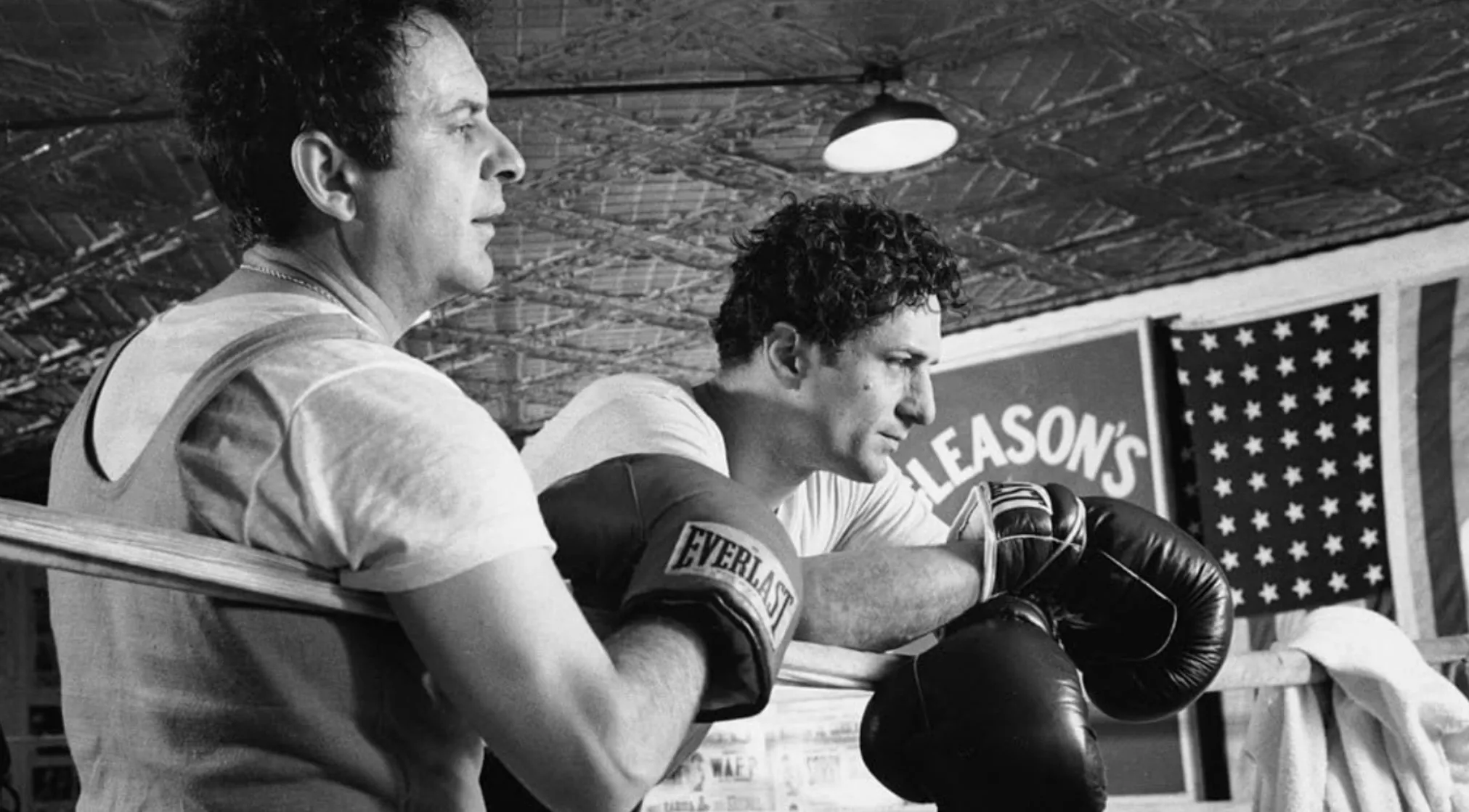 Black and white shot of Robert De Niro as boxer Jake LaMotta, wearing Everlast gloves, in a boxing ring.