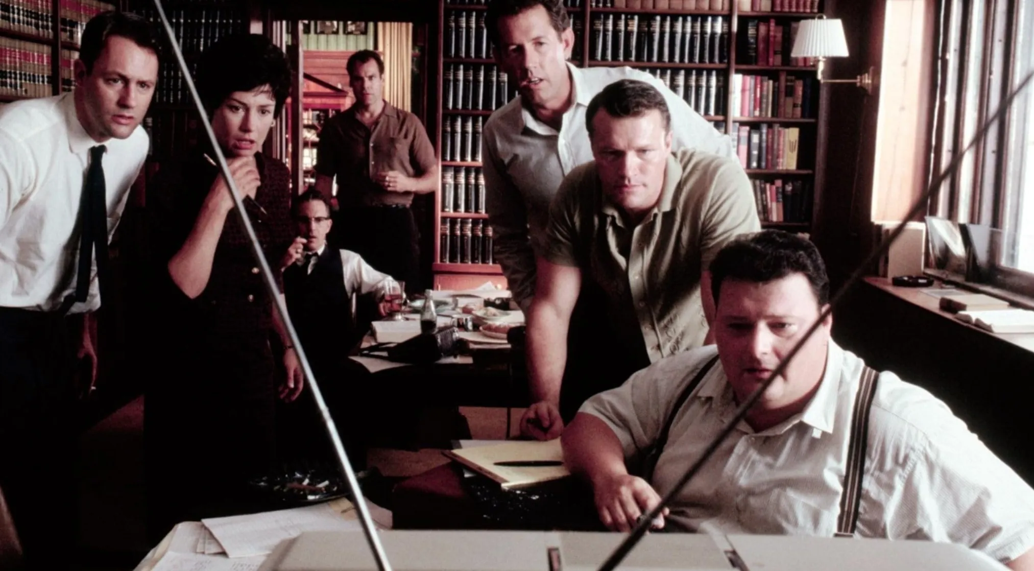 A group of people intently watching a TV, focused on a specific 80s & 90s General Movie Trivia moment from the film JFK.