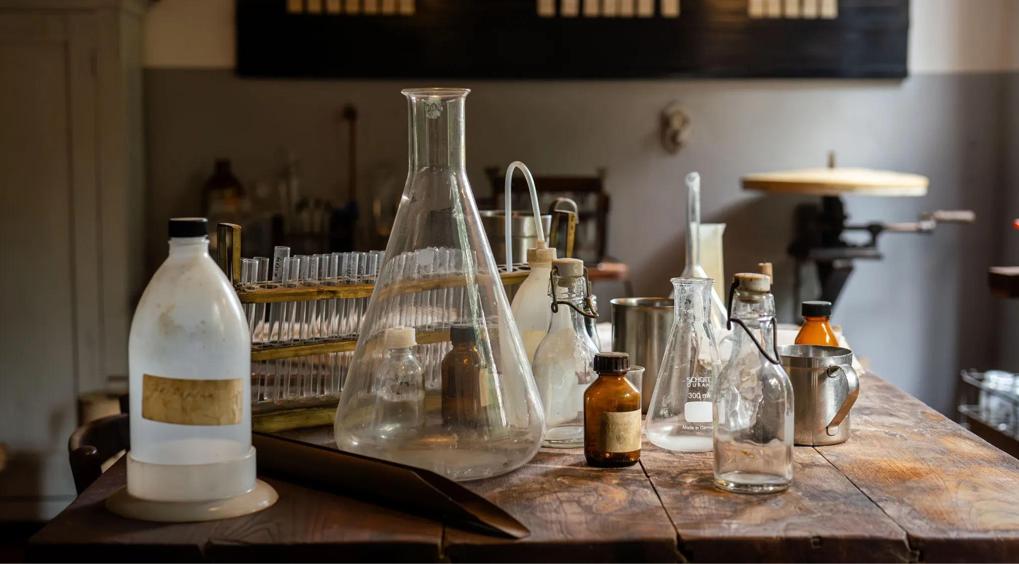 A vintage science lab setup with various glass beakers, test tubes, and bottles on a wooden table. Important for School Questions.