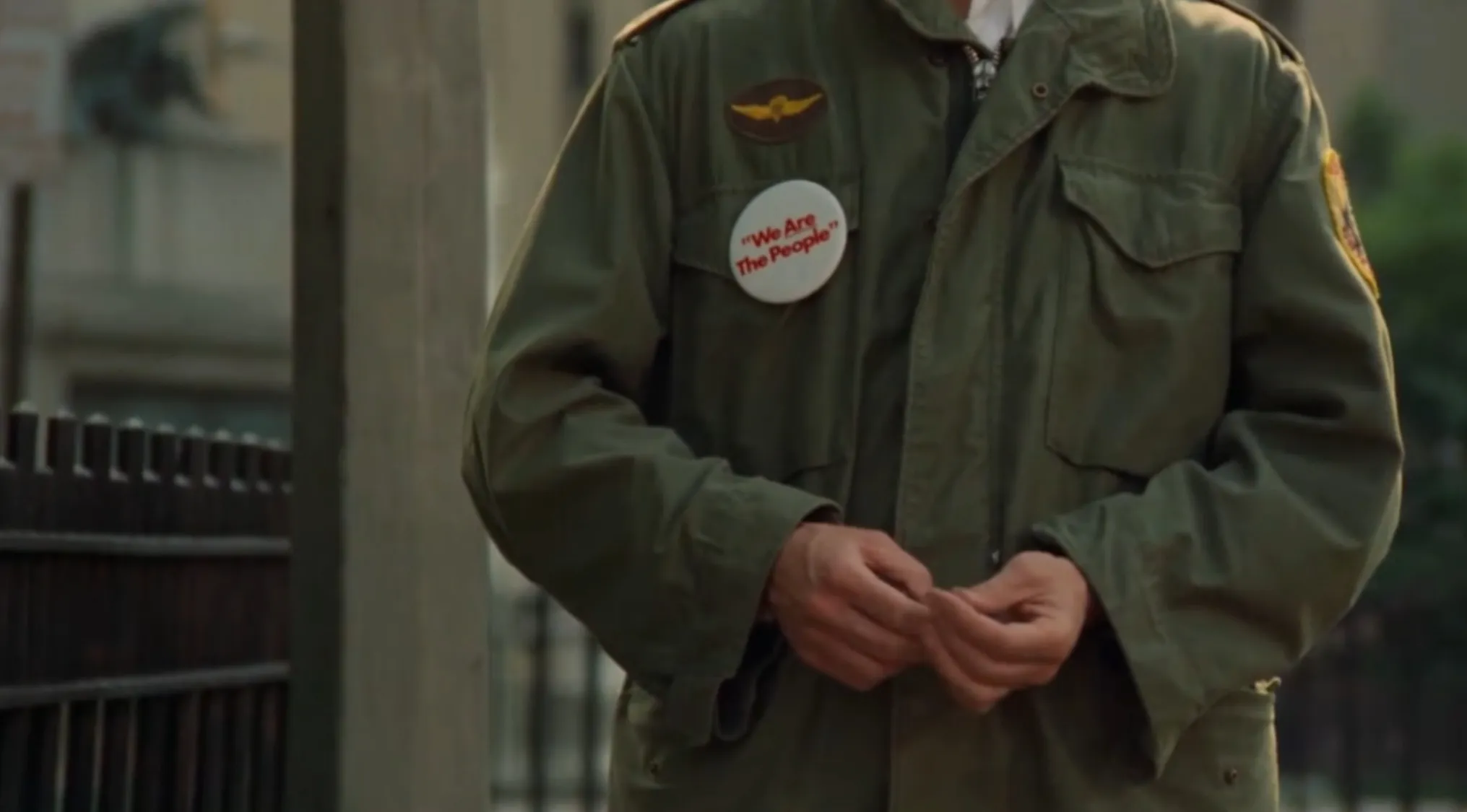 A close-up of a military-style jacket with a We Are the People button, part of iconic movie outfits.