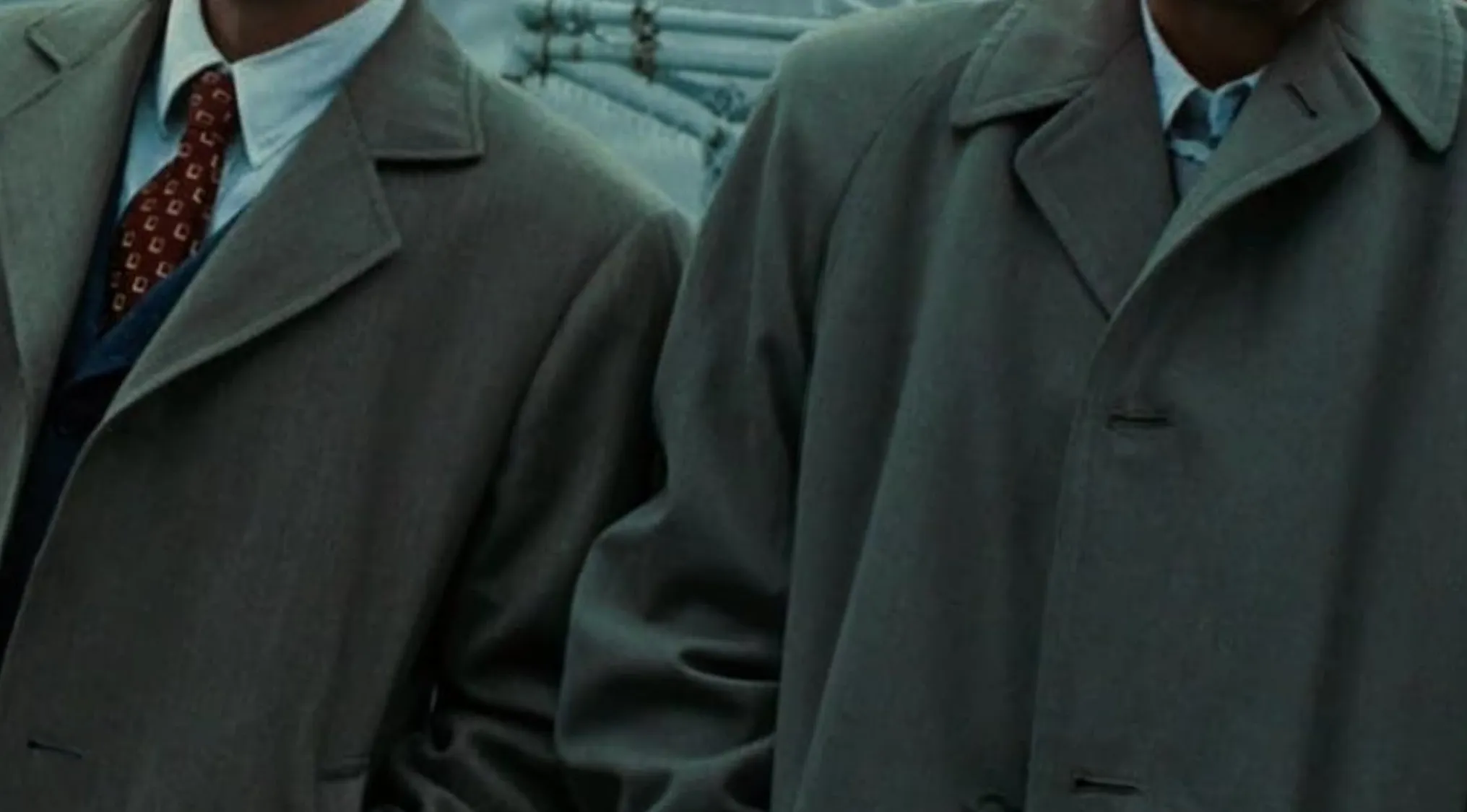Close-up of two men in classic movie outfits: fedoras and trench coats.