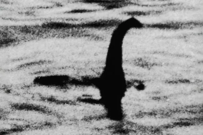 The infamous Loch Ness Monster, a dark silhouette, emerging from the water in a black and white photo.