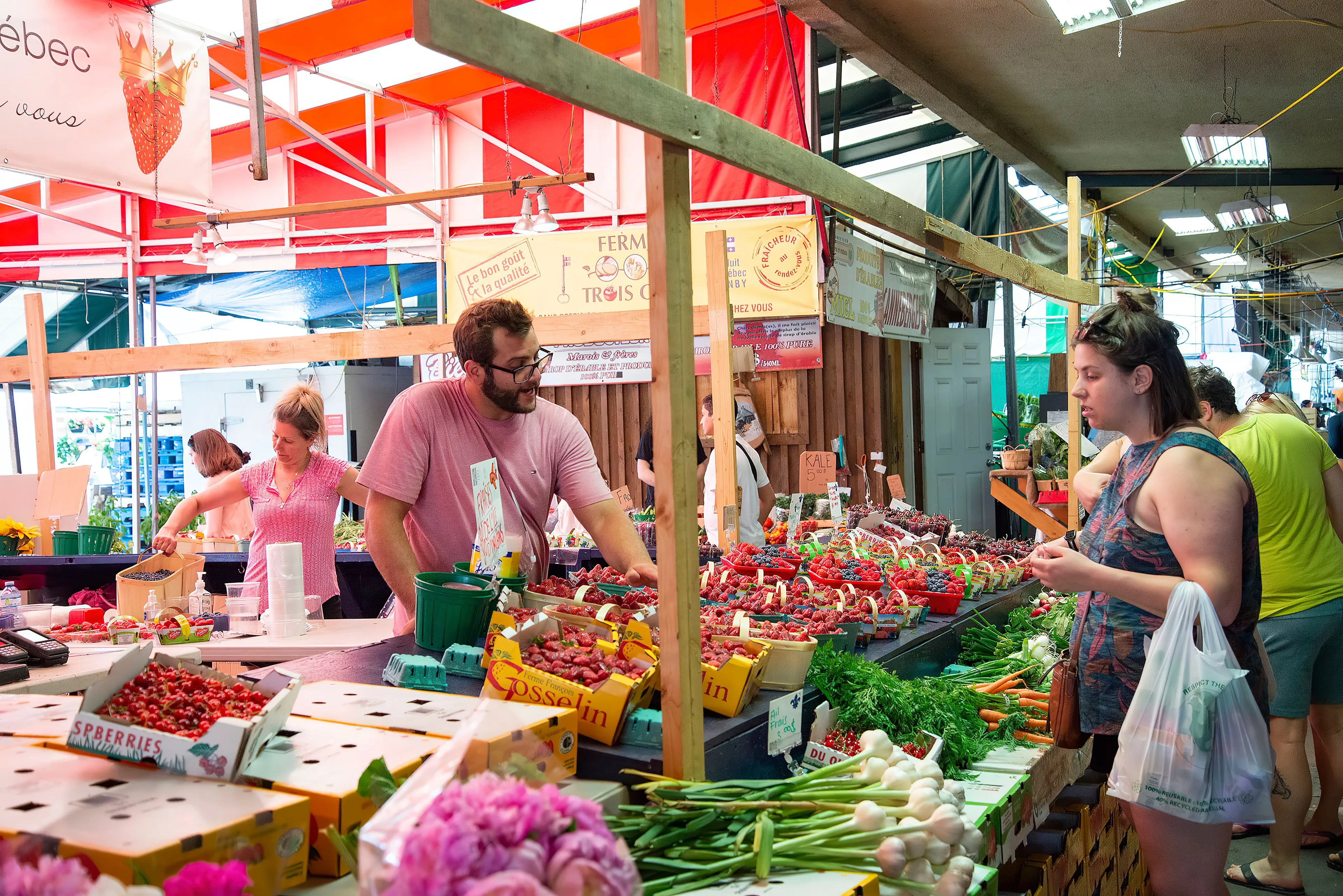 Customers at a farmers market buying fresh produce like berries and vegetables on a Sunday afternoon.