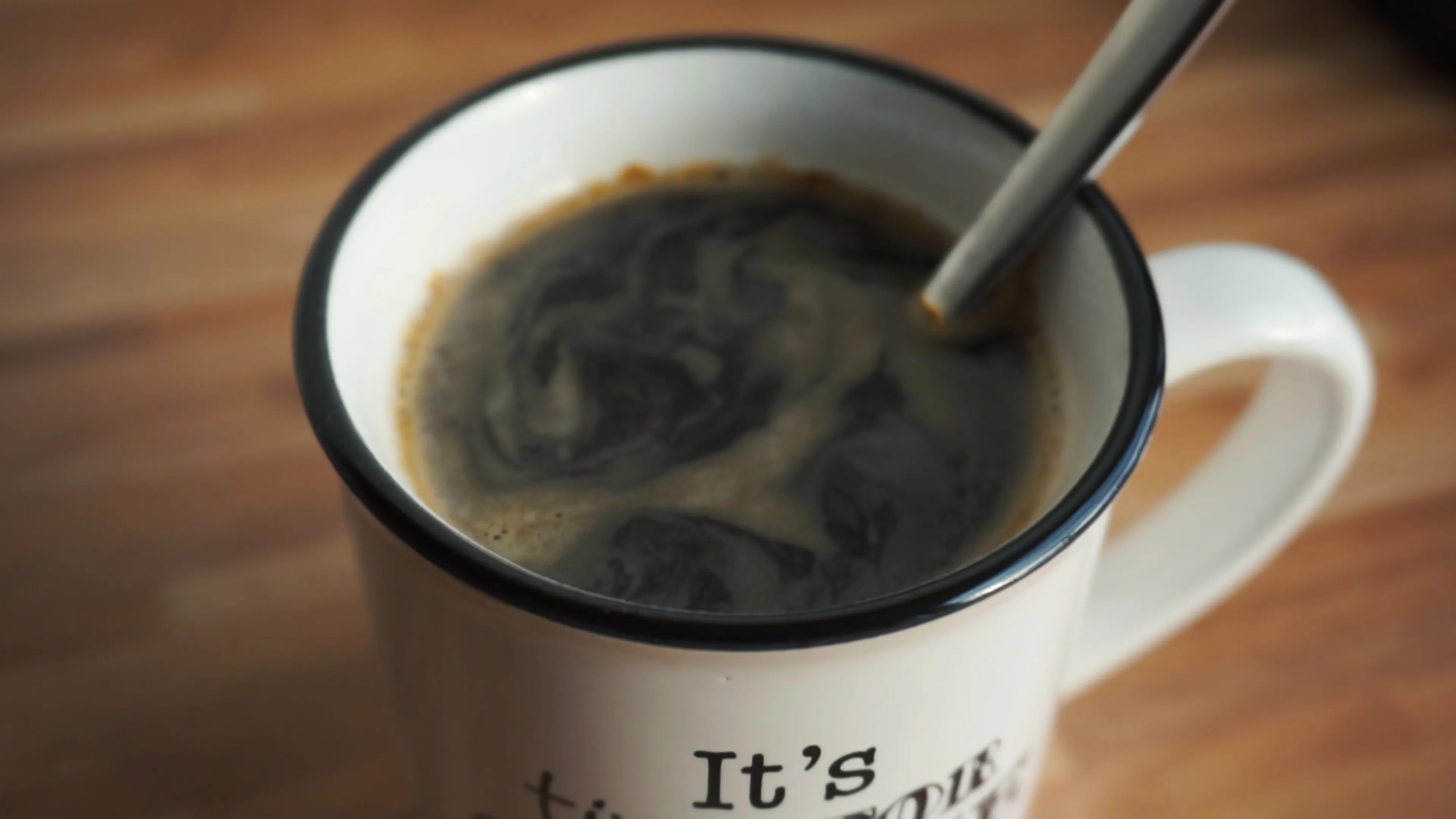 A close-up of a white mug filled with black coffee, with a spoon stirring the surface, for a drink choice.