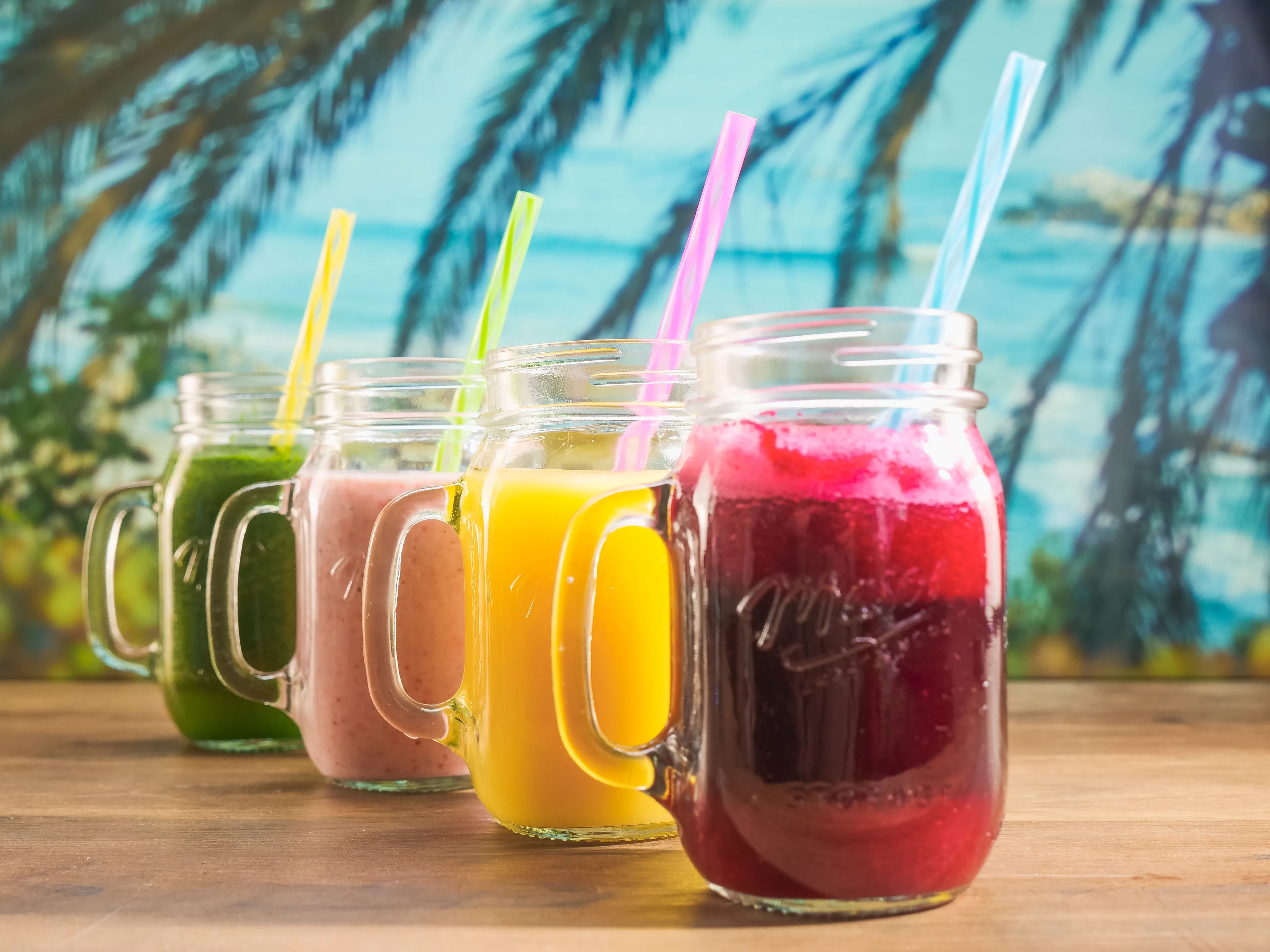 Vibrant colorful smoothies in mason jars with straws, a refreshing drink choice for a sunny day.