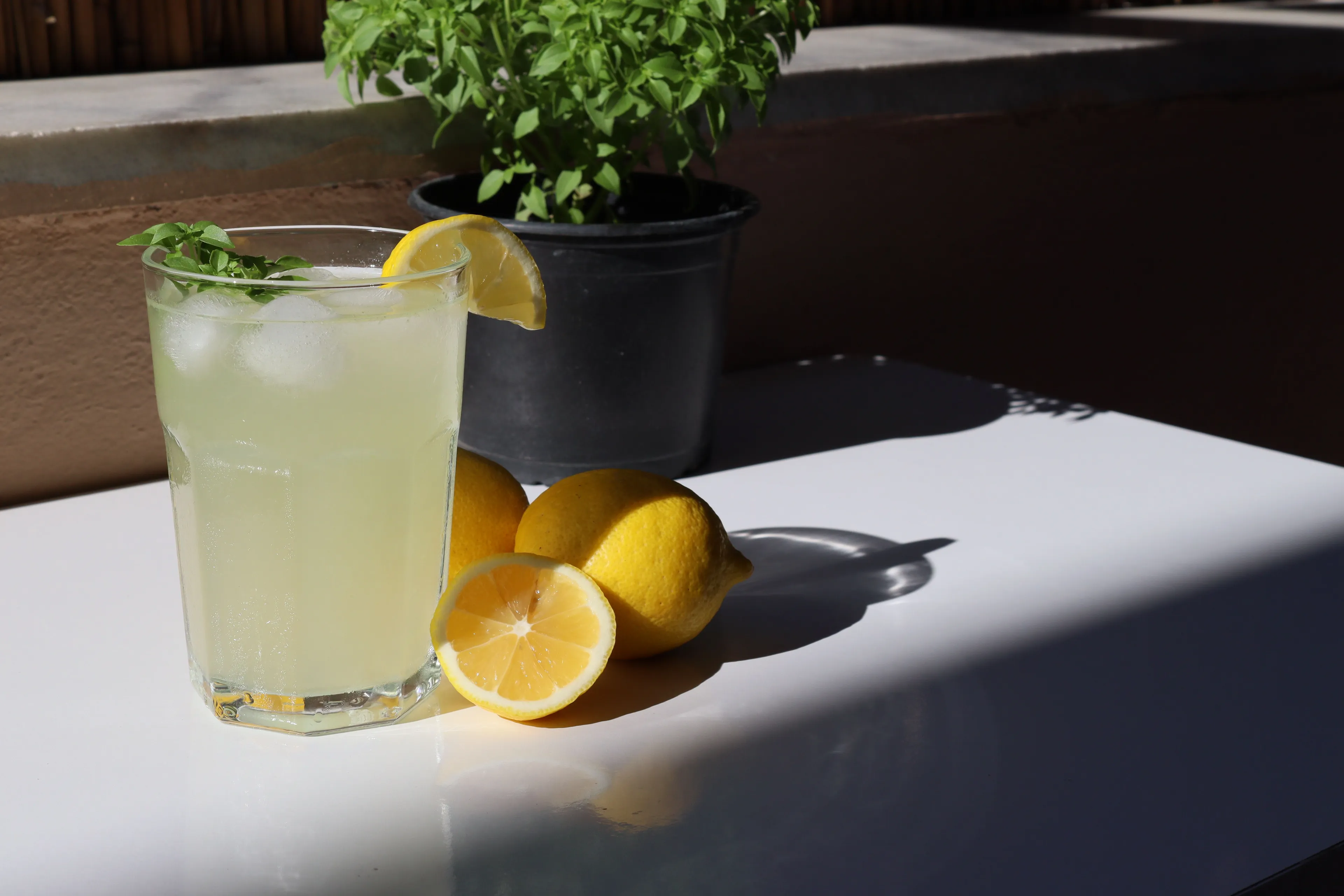 A glass of refreshing lemonade with ice and lemon slices on a table with fresh lemons.