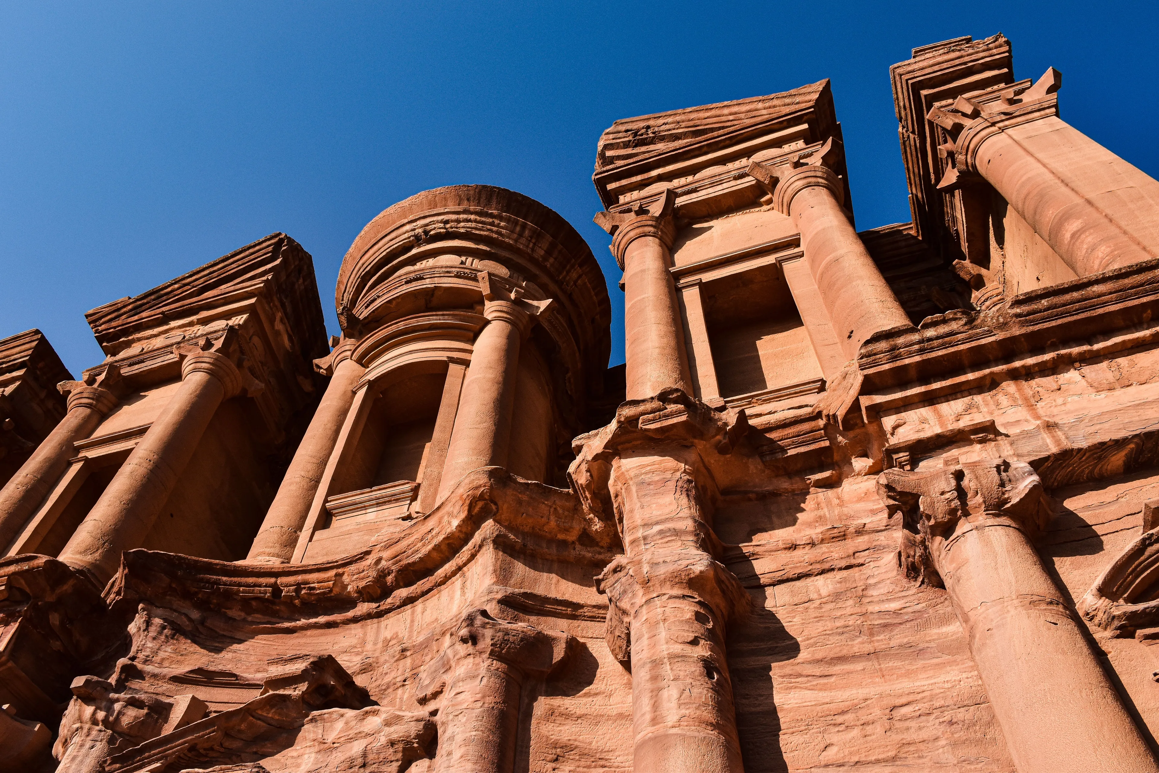 The ancient rock-cut architecture of Petra looms impressively against a bright blue sky, a stunning pick a place to visit.