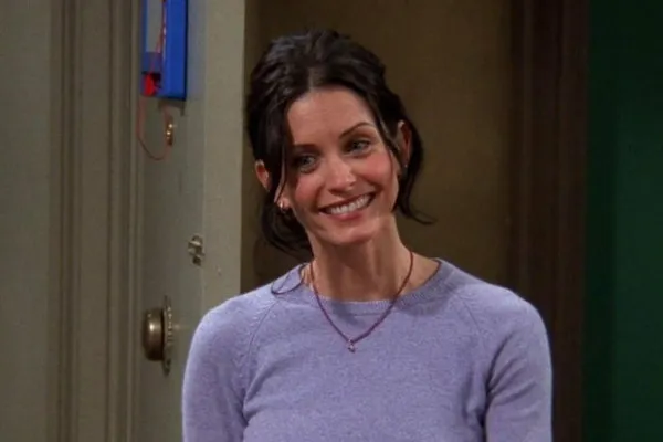 Monica Geller, smiling brightly in a light purple sweater, embodying the fictional character she slightly identifies with.