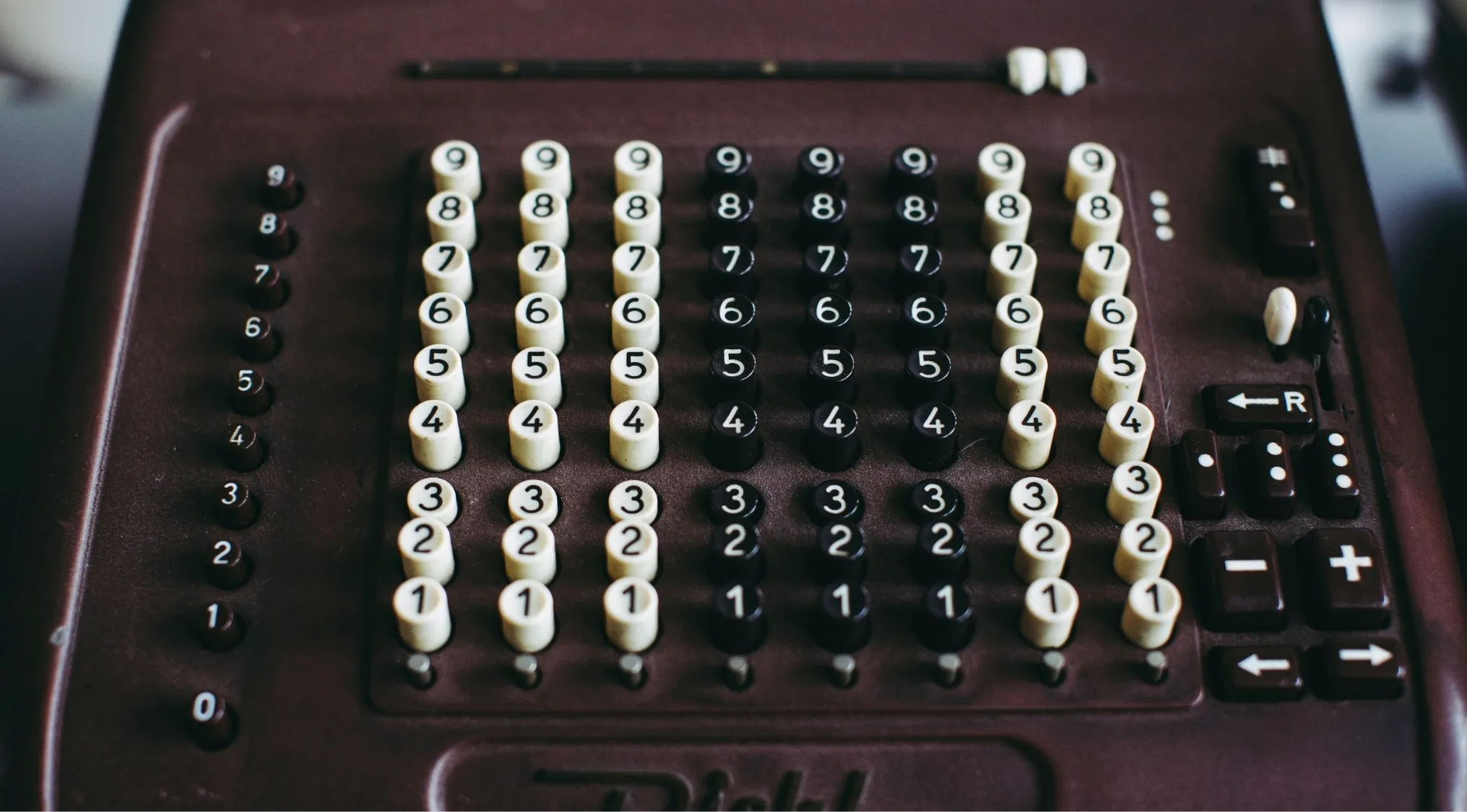 Close-up of an old mechanical calculator. The device, essential for understanding the Fundamental Rules of Arithmetic, features rows of number keys and input slots, in white and black.