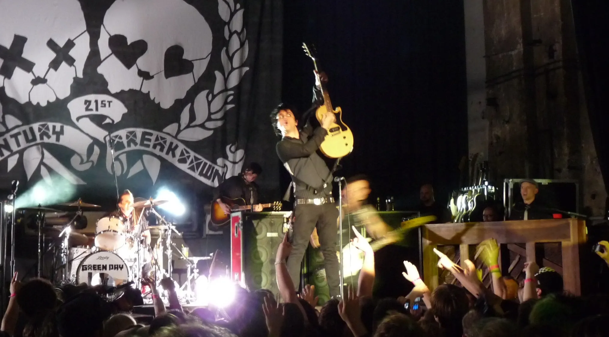 Green Day band performing live on stage, lead singer holding guitar up with music knowledge.