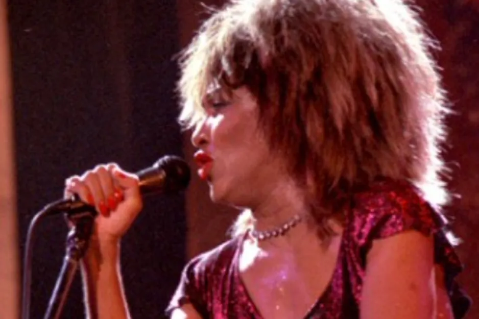 Tina Turner, a powerful performer known as the Queen of Soul, singing into a microphone on stage.