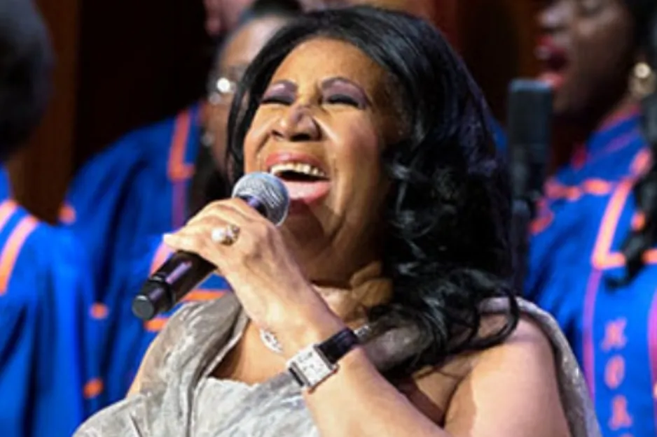 Aretha Franklin, the iconic Queen of Soul, performing live with a choir in the background.