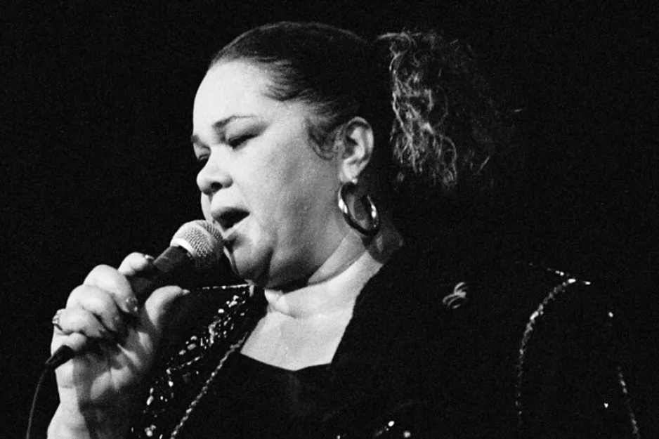 Etta James, known as the Queen of Soul, singing into a microphone in a black and white image.