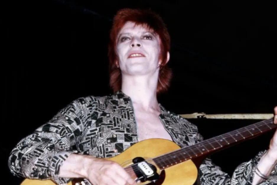 David Bowie as Ziggy Stardust, a famous singer alter ego, playing guitar on stage.