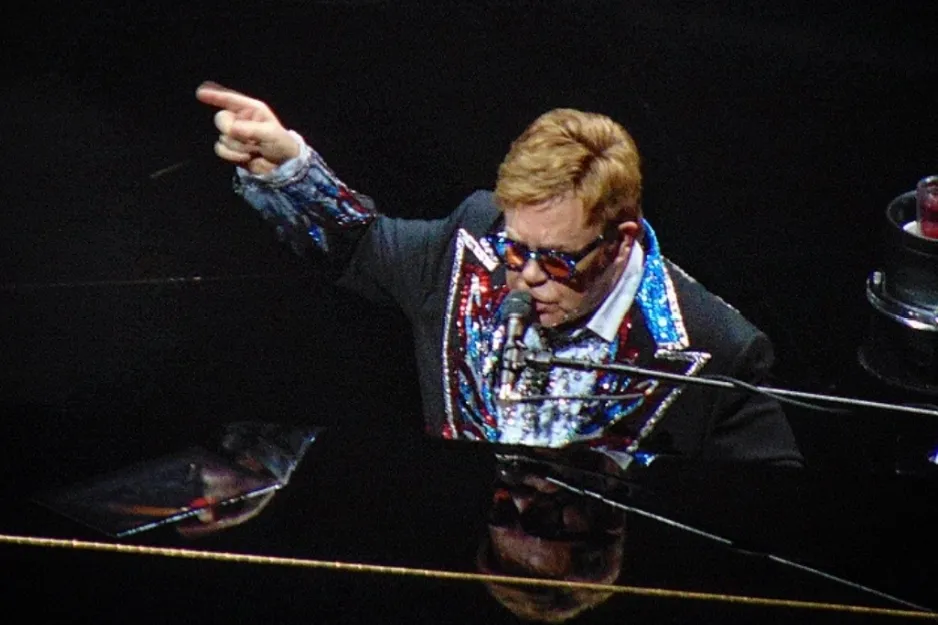 Elton John, a famous singer, performing at a piano on stage, wearing a sequined jacket.