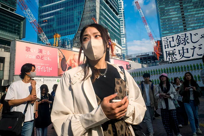 A woman in a face mask standing on a busy street in Japan, an ideal destination for street photographers.