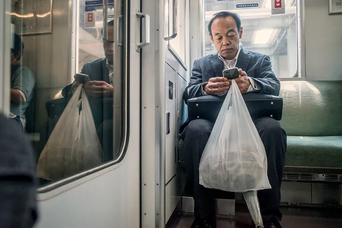 A man commuting on a train in Japan, checking his phone, a common sight for street photographers.