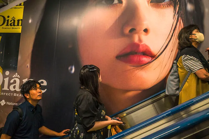 People on an escalator next to a large advertisement in Japan, perfect for street photographers capturing urban life.