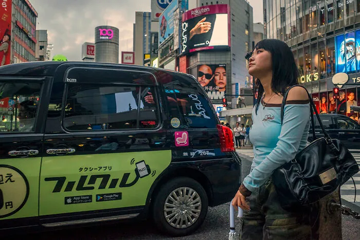 A woman standing beside a black taxi on a bustling street in Japan, a prime spot for street photographers.