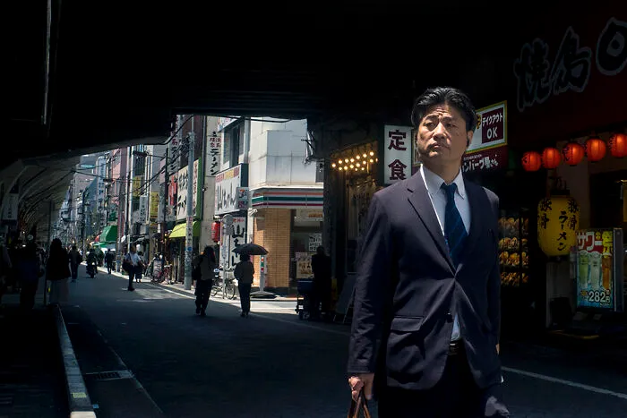 A man in a suit walking along a narrow street in Japan, an ideal destination for street photographers.